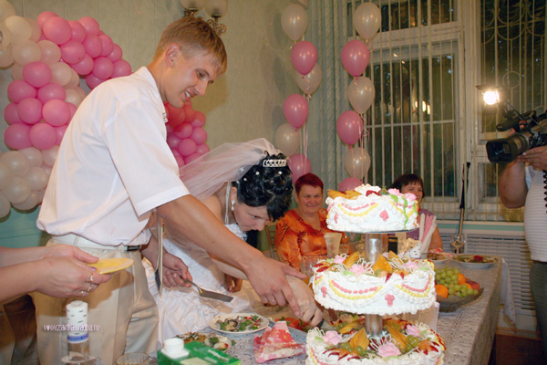 Разрезание свадебного торта на столе молодожёнов